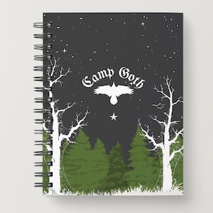 May include: Spiral-bound notebook with a dark gray cover featuring a forest scene. The design includes white trees, green pine trees, and the text "Camp Goth" with a raven and star. The background is a starry night.