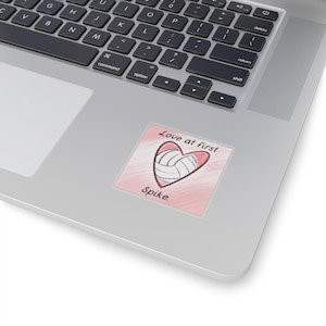 Puede incluir: Una pegatina rosa y blanca con un balón de voleibol dentro de un corazón. El texto "Love at first Spike." está debajo del corazón.