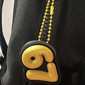 May include: Black backpack with a yellow zipper pull featuring the number "69" in a 3D design. The zipper pull is yellow and black, and the backpack has a black zipper.