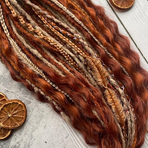 May include: A set of brown, blonde, and beige synthetic dreadlocks with wavy textures. The dreadlocks are arranged in a loose bundle.