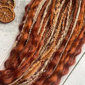 May include: A set of long, wavy synthetic dreadlocks in shades of auburn, brown, and beige. The dreadlocks are arranged in a loose, flowing style.