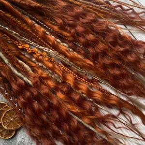May include: A set of synthetic dreadlocks in shades of brown, blonde, and orange. The dreadlocks are wavy and have a natural, bohemian look.
