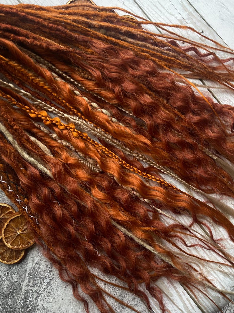 May include: A set of synthetic dreadlocks in shades of brown, blonde, and orange. The dreadlocks are wavy and have a natural, bohemian look.