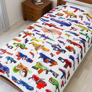May include: A white twin-sized bedspread with a colorful pattern of toy guns. The guns are in various colors, including blue, red, orange, green, and yellow. The bedspread is made of a soft, comfortable fabric.
