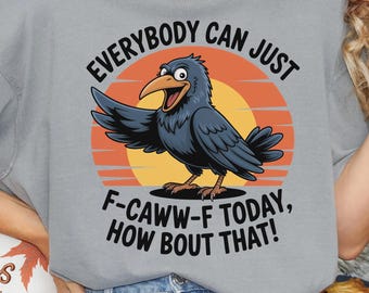 Pode incluir: Uma camiseta cinza com um desenho de corvo e o texto "EVERYBODY CAN JUST F-CAWW-F TODAY, HOW BOUT THAT!". O corvo está situado em frente a um design de pôr do sol. A camiseta faz parte de uma coleção de outono.