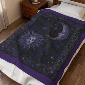 May include: A rectangular throw blanket featuring a dark purple and black celestial design. The center displays a sun and a crescent moon with human-like faces surrounded by stars. A decorative border with intricate scrollwork frames the image.