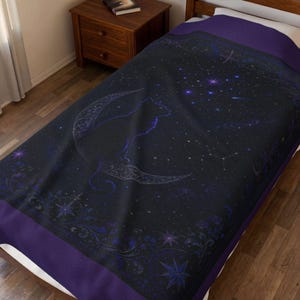 Puede incluir: Una colcha de color morado oscuro y negro con un dise&ntilde;o celestial que muestra la silueta de un gato sentado sobre una luna creciente. La tela presenta un patr&oacute;n de cielo nocturno estrellado con bordes de volutas florales y estrellas.