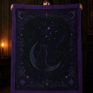 Puede incluir: Una manta rectangular con un gato negro sentado sobre una luna creciente contra un cielo nocturno estrellado en negro y morado oscuro. El dise&ntilde;o incluye bordes florales intrincados, constelaciones y elementos celestiales en tonos morados.