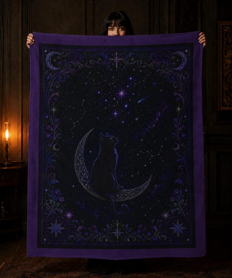 Puede incluir: Una manta rectangular con un gato negro sentado sobre una luna creciente contra un cielo nocturno estrellado en negro y morado oscuro. El dise&ntilde;o incluye bordes florales intrincados, constelaciones y elementos celestiales en tonos morados.
