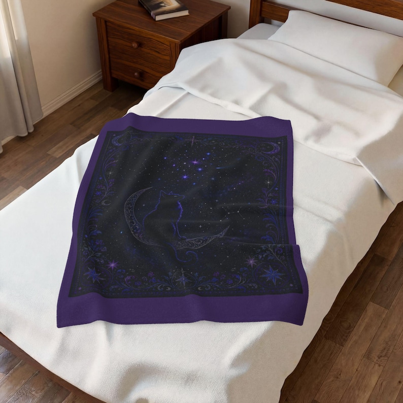 Puede incluir: Una manta rectangular con un borde morado oscuro y un centro negro. El dise&ntilde;o muestra la silueta de un gato sentado sobre una luna creciente, rodeado de estrellas azules y moradas, constelaciones y patrones de enredaderas florales.