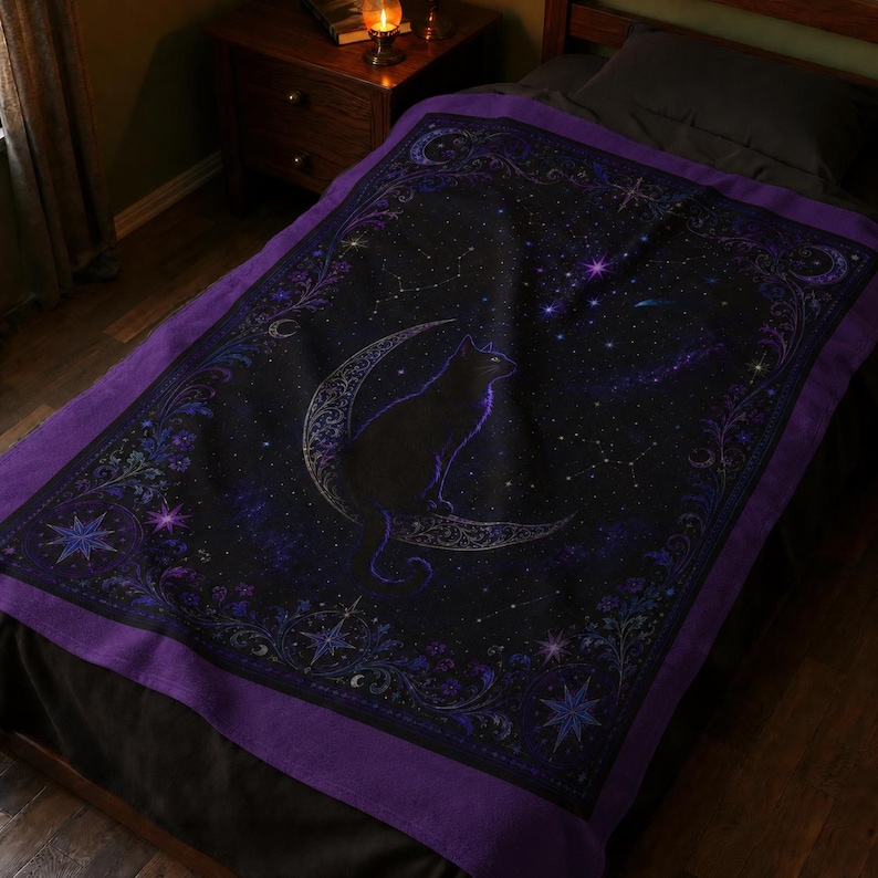 Puede incluir: Una manta rectangular con fondo negro que presenta la silueta central de un gato sentado sobre una luna creciente. El dise&ntilde;o incluye patrones celestiales en azul y morado, estrellas y un borde floral decorativo en tonos violetas.