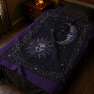 May include: A rectangular throw blanket featuring a dark purple and black celestial design. The center displays a stylized sun face and a crescent moon face surrounded by stars and constellations. A decorative border frames the entire image.