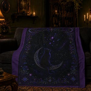 Puede incluir: Una manta rectangular con un borde morado oscuro y un campo central negro. El dise&ntilde;o muestra la silueta de un gato sentado sobre una luna creciente rodeado de estrellas, constelaciones y complejos patrones de volutas florales.