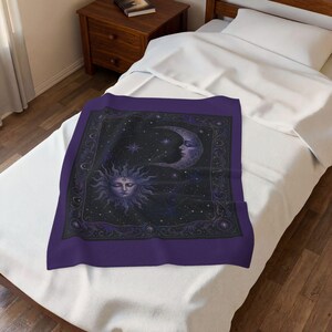 May include: A rectangular purple throw blanket featuring a central black square panel with a detailed illustration of a sun and a crescent moon with human faces, surrounded by a dark border with intricate filigree patterns and small stars.
