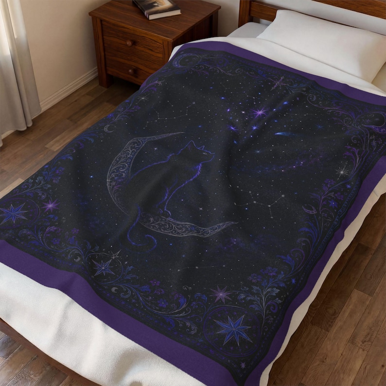 Puede incluir: Una manta de color negro y morado oscuro con un dise&ntilde;o celestial que muestra la silueta de un gato sentado sobre una luna creciente. El patr&oacute;n incluye bordes florales intrincados, estrellas dispersas y constelaciones sobre un cielo nocturno.