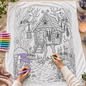 Puede incluir: Una manta de tela blanca con una ilustración de líneas negras de una cabaña sobre patas de pollo en un entorno forestal con setas, calaveras y pájaros. El diseño incluye una linterna colgante y hierbas secas para colorear.