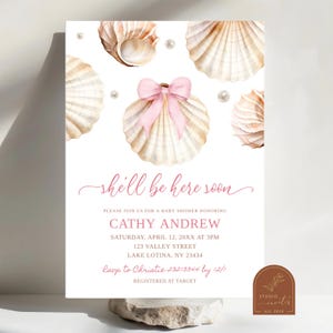 Puede incluir: Una invitación a una fiesta de bienvenida al bebé con un tema de conchas marinas rosas y blancas. La invitación presenta una concha con un lazo rosa y perlas. El texto de la invitación dice "Ella estará aquí pronto" e incluye los detalles de la fiesta de bienvenida al bebé, incluida la fecha, la hora, la ubicación y la información de RSVP.