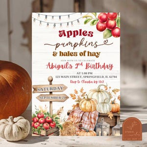 May include: A birthday invitation card featuring a white wood background with string lights, red apples, and pumpkins. Text reads: Apples pumpkins & bales of hay, Abigail's 2nd Birthday, at 1:00 PM, 123 Main Street, Springfield, IL 62704, RSVP to Claudia by 12/12.