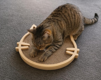 Puede incluir: Un gato atigrado descansa sobre un rascador con forma de gato. El rascador es de cartón y tiene un marco de madera. El gato es marrón y beige con rayas. Es un accesorio para gatos.