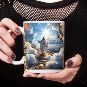 May include: A white ceramic mug featuring a printed graphic of a figure in a robe walking toward a bright sun and a cross. The image is framed by a jagged, stone-like border that creates a 3D effect against a sky filled with clouds and light.