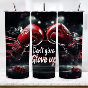 May include: A cylindrical tumbler with a metal straw featuring a graphic of red boxing gloves in a dark ring. The text "Don't give Glove up" is printed in white and red lettering. The design includes smoke effects and red ropes in the background.
