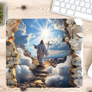 May include: A square mouse pad featuring a graphic illustration of a figure in a robe walking toward a bright sunlit sky while holding a wooden cross. The scene is framed by a cracked stone wall effect with white clouds and rocky terrain.