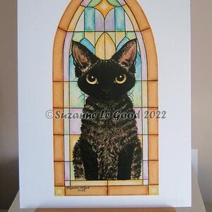 May include: A black cat with green eyes sits inside a stained glass window. The window is a pointed arch with a yellow frame and colourful glass panels. The cat is looking directly at the viewer. The text "Suzanne Le Good 2022" is printed in the lower right corner of the image.