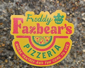 May include: Yellow and red sticker with the text "Freddy Fazbear's Pizzeria" and the words "Where fantasy and fun come to life". A green and red pizza slice is in the middle of the sticker.