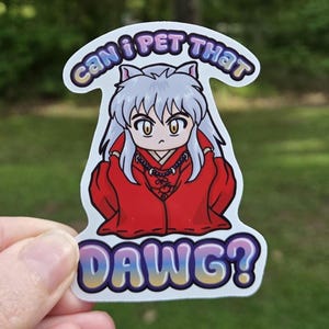 May include: A die-cut sticker featuring a chibi-style anime character with long white hair and dog ears, wearing a red robe and a beaded necklace. The text above reads CAN I PET THAT and the text below reads DAWG? in a purple and yellow gradient.