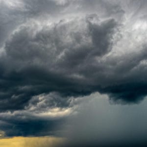 May include: A dramatic sky with dark, stormy clouds forming a thick, ominous layer. The clouds are a deep gray, with hints of lighter gray and white in the background. The sky is overcast, with no visible sun or blue sky.