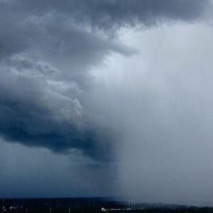 May include: A dark, stormy sky with a large, ominous cloud hanging low in the distance. Rain is falling from the cloud, creating a curtain of water.