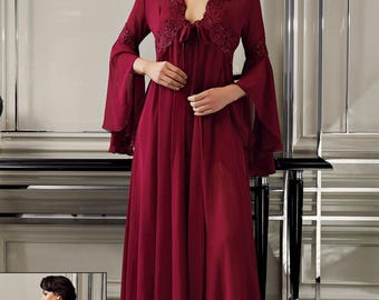 May include: A burgundy-coloured, long-sleeved robe with a V-neckline and bell sleeves. The robe features lace detailing around the neckline and cuffs. The fabric appears to be a lightweight, flowing material. The robe is floor-length.