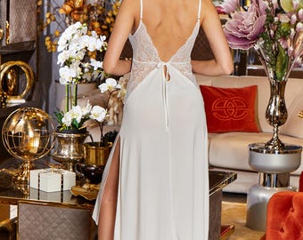 May include: White satin slip dress with a lace back and a side slit. The dress is tied at the back with a satin ribbon.