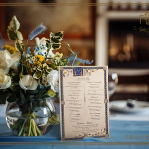 May include: A table setting with a floral arrangement and a menu. The menu is beige with blue and gold accents, listing courses in English and French. The floral arrangement includes white roses, yellow flowers, and blue accents in a clear glass bowl.