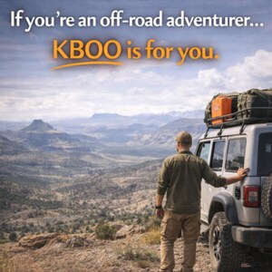 May include: A person stands next to a silver off-road vehicle with gear on the roof, overlooking a mountainous landscape. The text "If you're an off-road adventurer... KBOO is for you" is displayed in the upper portion of the image.