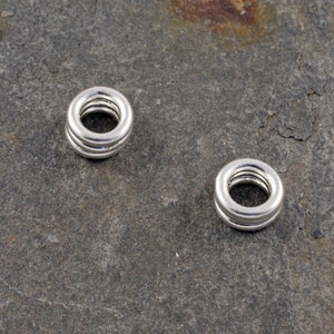 May include: Two silver jump rings, each with three concentric circles, are shown on a grey textured surface.