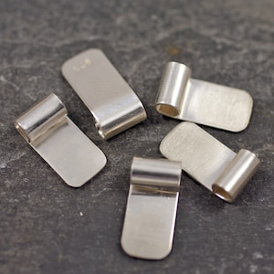 May include: Five silver-toned metal pendant bails with a rectangular shape and a rolled edge. The bails are designed to be used for attaching pendants to necklaces or bracelets.