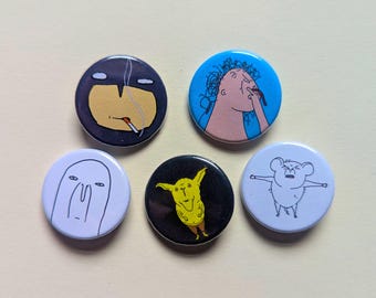 May include: A set of five circular pin-back badges featuring various cartoon illustrations. The designs include a dark figure smoking, a person picking their nose on blue, a simple white face, a yellow creature on black, and a small white animal.