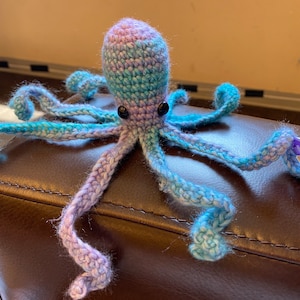 May include: A crocheted octopus toy with a purple and blue ombre color scheme. The octopus has eight tentacles and black eyes.
