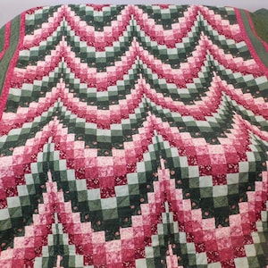 May include: A green and pink quilt with a geometric pattern. The quilt is made of squares and rectangles, and the pattern is repeated throughout the quilt.