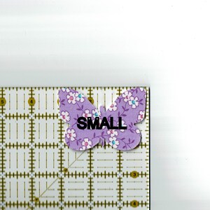 May include: A purple butterfly fabric applique with white flowers and the word "SMALL" printed on it.