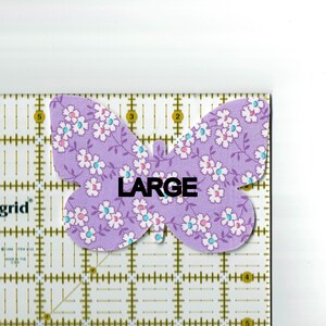 May include: A purple butterfly-shaped fabric patch with a white floral pattern and the word "LARGE" printed in black.