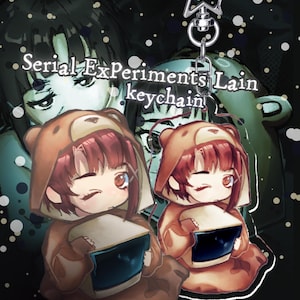 May include: A keychain featuring two anime-style characters in bear costumes, holding a screen. The text "Serial Experiments Lain keychain" is above the characters. The background is dark with a green and black color scheme.