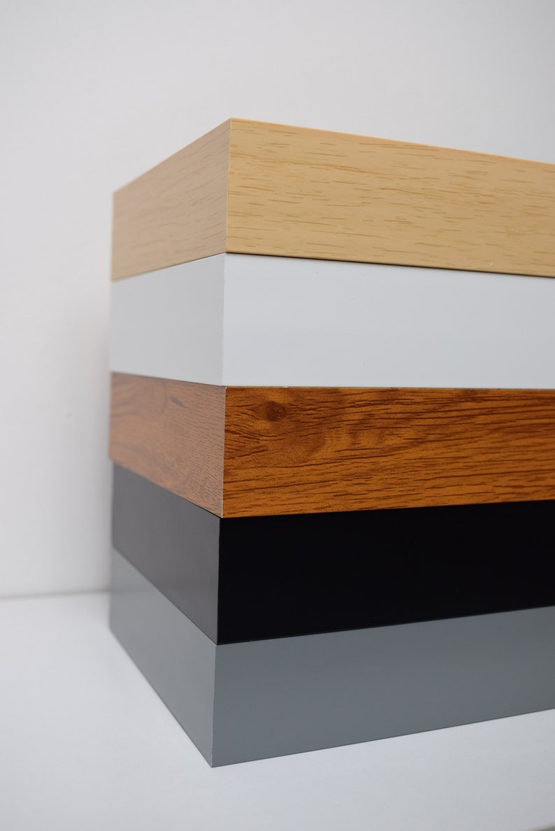 May include: A stack of five wooden picture frames in different colors. The top frame is light wood, followed by white, brown, black, and gray.