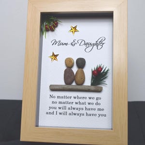 May include: A framed artwork featuring a pebble art design of two figures, representing a mother and daughter, with the text "Mum & Daughter" and a poem about their bond. The artwork is set against a white background with gold stars and a sprig of greenery with red berries.