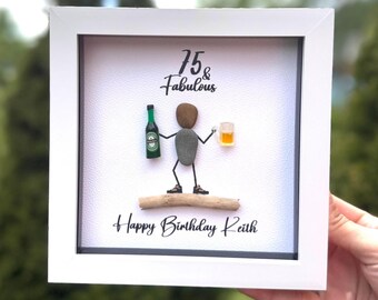 Op de afbeelding: Een ingelijst kunstwerk met een witte rand. Het toont een kiezelkunstfiguur met een bierfles en een bierglas. De tekst "75 & Fabulous" en "Happy Birthday Keith" staat op het kunstwerk.