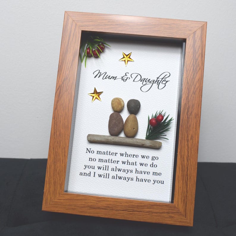 May include: Framed artwork featuring a pebble art design of two figures sitting on a piece of driftwood. The artwork includes red berries, green foliage, and gold stars. The text reads "Mum & Daughter" and "No matter where we go, no matter what we do, you will always have me and I will always have you."