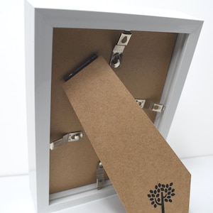 May include: White picture frame with a brown cardboard backing. The backing has a small tree logo and the text "Nicola Spring" printed on it.