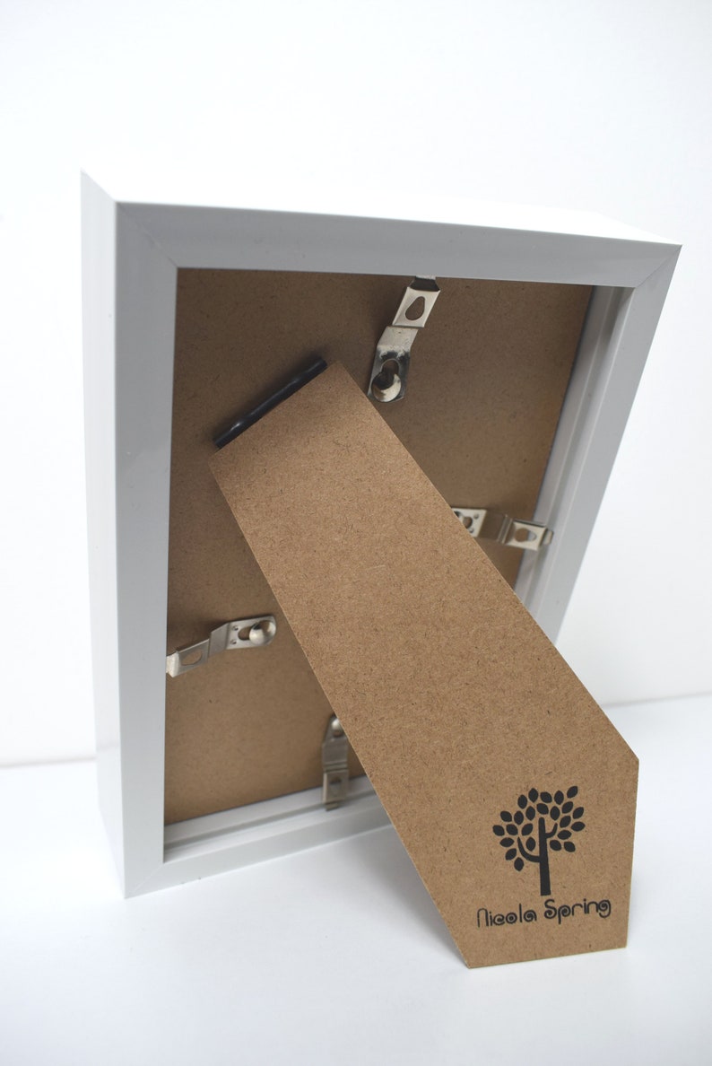 May include: White picture frame with a brown cardboard backing. The backing has a small tree logo and the text "Nicola Spring" printed on it.