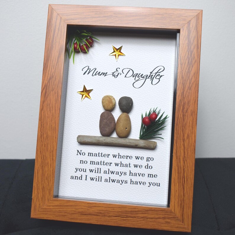 May include: A framed artwork featuring a pebble art design of two figures sitting on a driftwood log. The artwork has a white background with the text "Mum & Daughter" and a quote: "No matter where we go, no matter what we do, you will always have me and I will always have you".